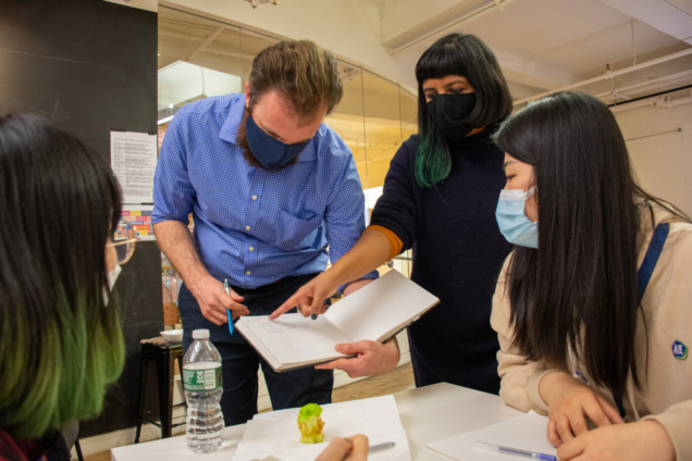 two instructors showing students text in an open book