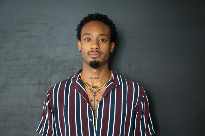 DiMitri Martin wearing a striped crimson and navy shirt looking at the camera